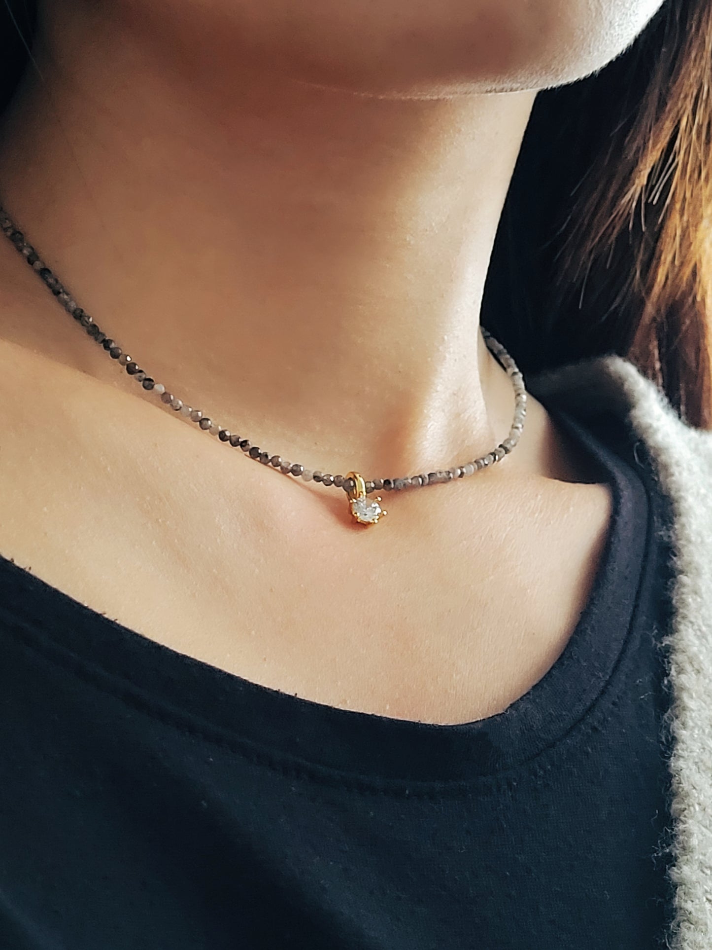 Close-up of a labradorite beaded necklace with a detachable diamond charm, worn around a woman neck in minimalist elegance style.