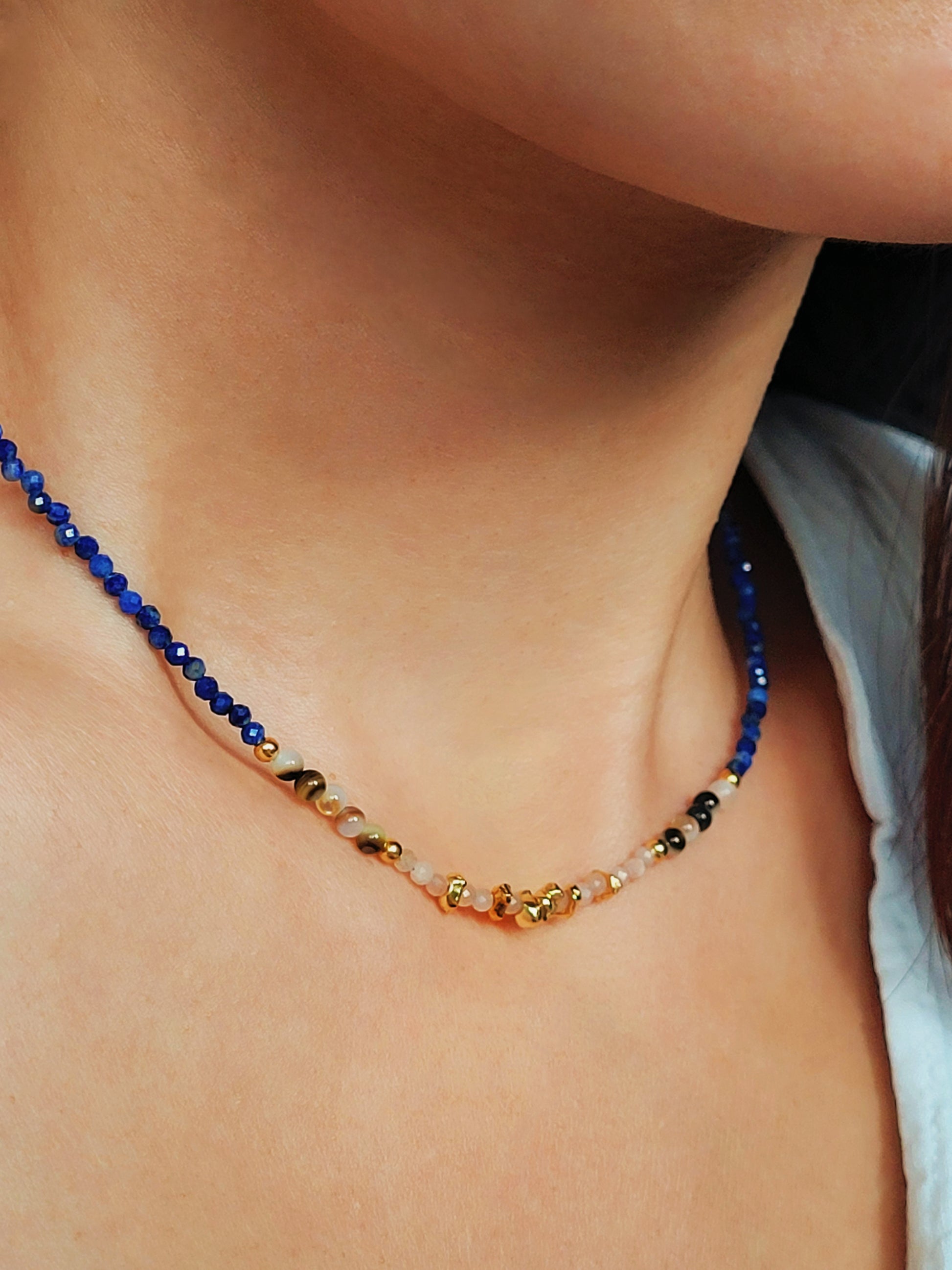 Close up of a woman wearing blue lapis lazuli beaded necklace featuring a mix of gemstones and elegant gold vermeil beads. Handcrafted for a unique, luxurious look. Perfect for any occasion. Stand out in style with this exquisite piece!