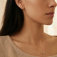 Close-up of a woman wearing Leo earrings and a Leo necklace against a neutral background