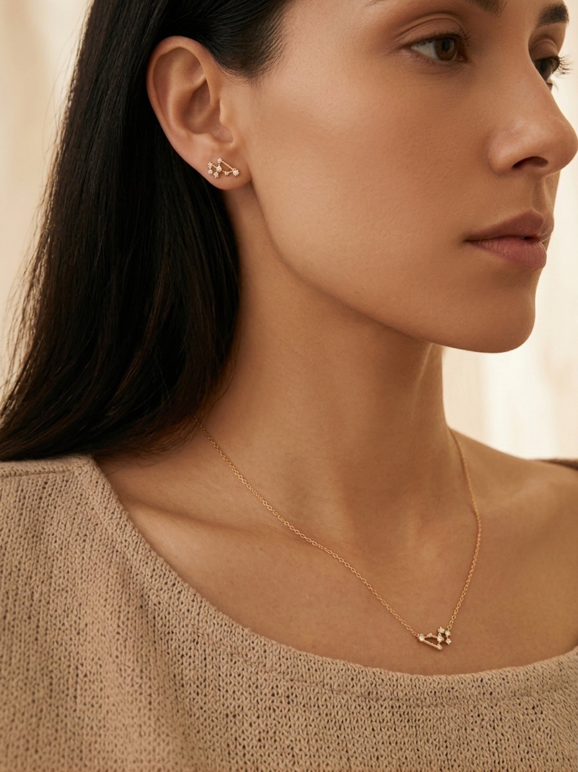 Close-up of a woman wearing Leo earrings and a Leo necklace against a neutral background