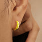 A gold-coloured hoop earring with a yellow enamel design. The earring is a small, curved shape, with a bright yellow colour on the outer edge and a black accent. The earring is worn on the ear.