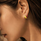 A close-up of an ear with a small gold hoop earring. The earring has a bright wave pattern yellow enamel with simple, modern design, suitable for everyday wear.