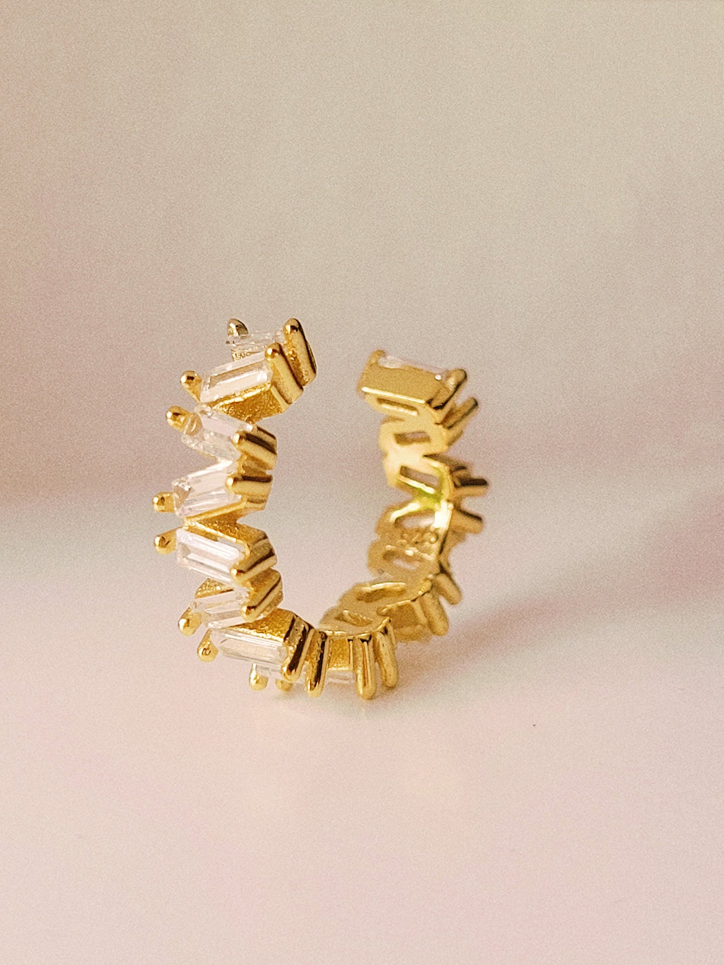 18ct gold vermeil ear cuff featuring a sleek, open design with multiple clear baguette-cut gemstones. The cuff has a modern, minimalist style and does not require piercing, making it a versatile accessory for cartilage or earlobe wear.