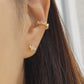 Close-up of a woman's ear wearing a gold vermeil ear cuff with baguette-cut stones, showcasing its modern, geometric design. Paired with a small stud earring in a floral pattern, the cuff sits comfortably on the upper ear without needing a piercing.