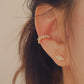 Close-up of a woman's ear wearing a gold vermeil ear cuff with baguette-cut stones, showcasing its modern, geometric design. Paired with a small stud earring in a floral pattern, the cuff sits comfortably on the upper ear without needing a piercing.