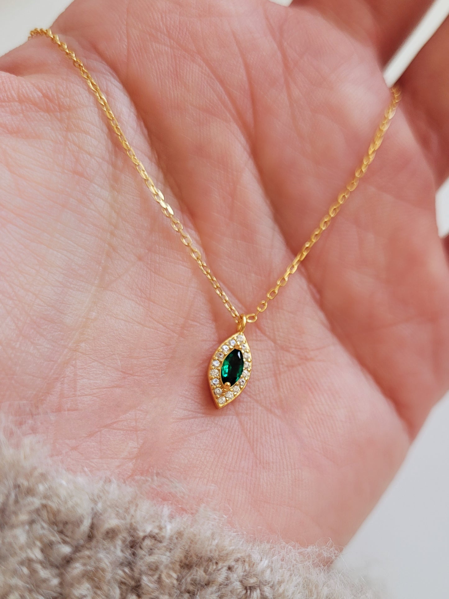 Close-up of a marquise emerald green evil eye pendant necklace on a delicate gold chain, showcasing its dainty and elegant vintage-inspired design.