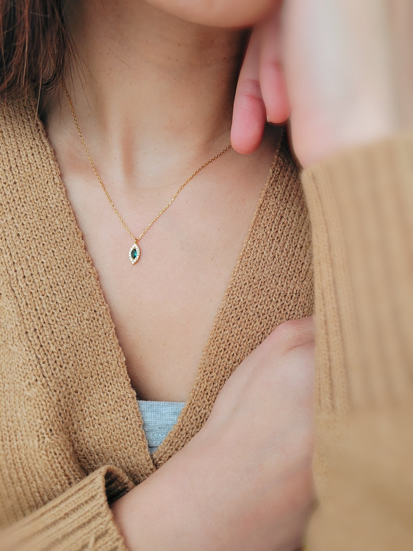 Close-up of a marquise emerald green evil eye pendant necklace on a delicate gold chain, showcasing its dainty and elegant vintage-inspired design.