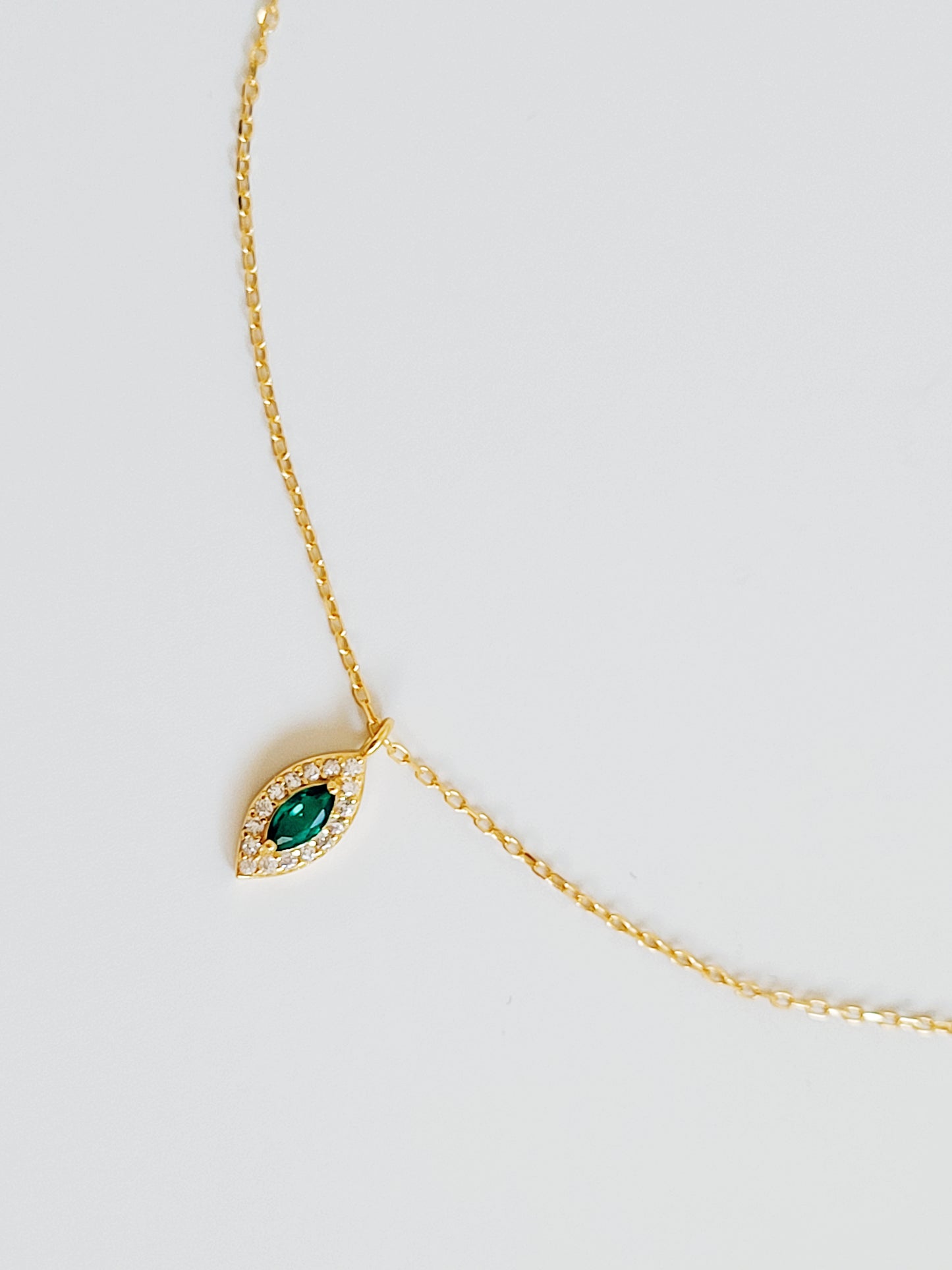 Close-up of a marquise emerald green evil eye pendant necklace on a delicate gold chain, showcasing its dainty and elegant vintage-inspired design.