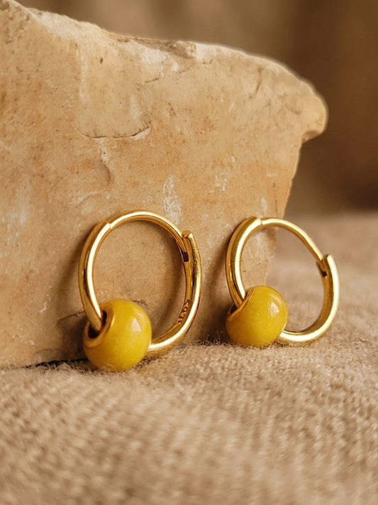 Close-up of mini yellow enamel bead huggie earrings in 18k gold plating, featuring a delicate handpainted bobble design on a small gold hoop.