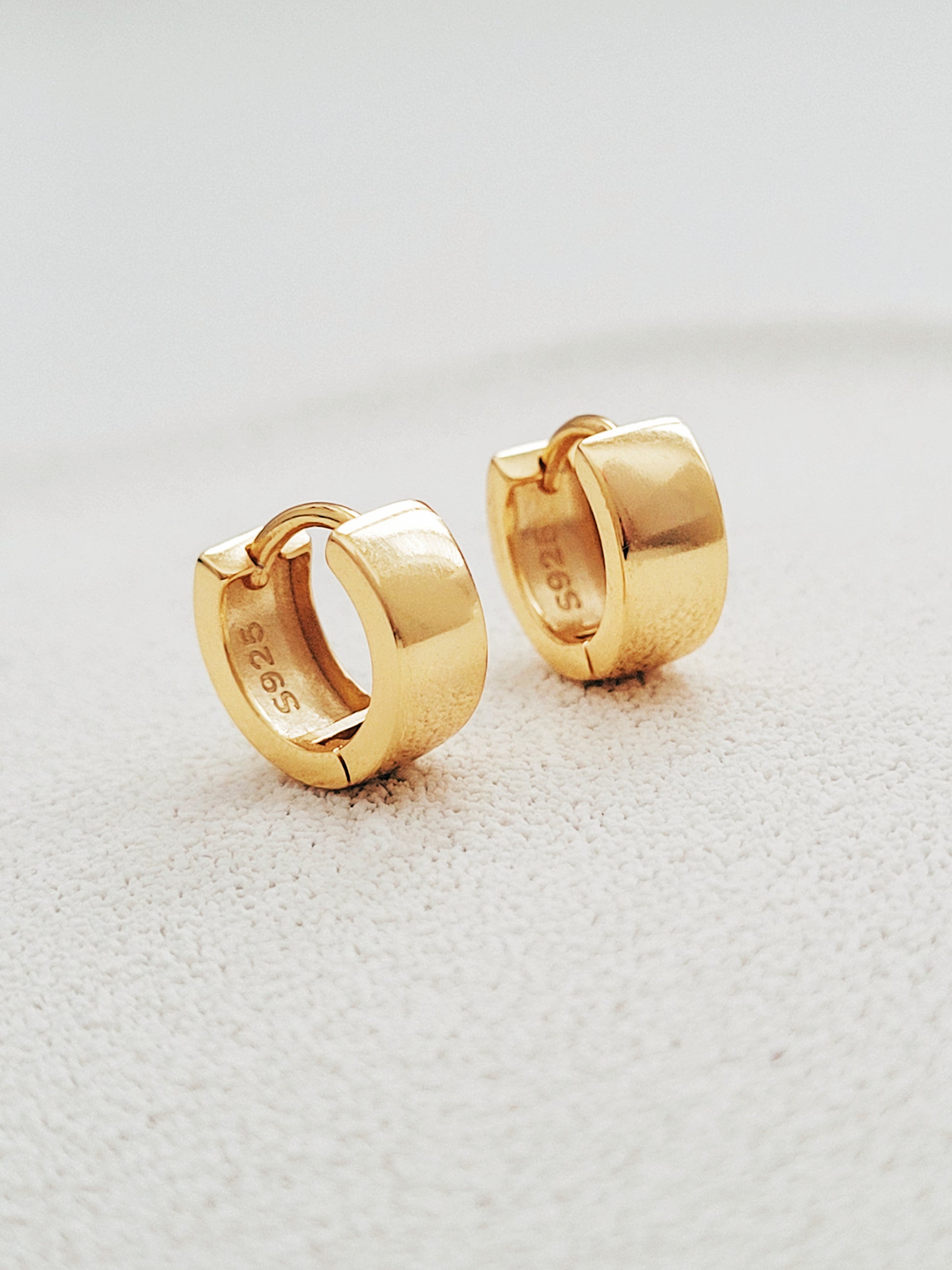 Stylish and minimalist chunky small gold hoop earrings displayed on a white surface showcasing their versatile design. 