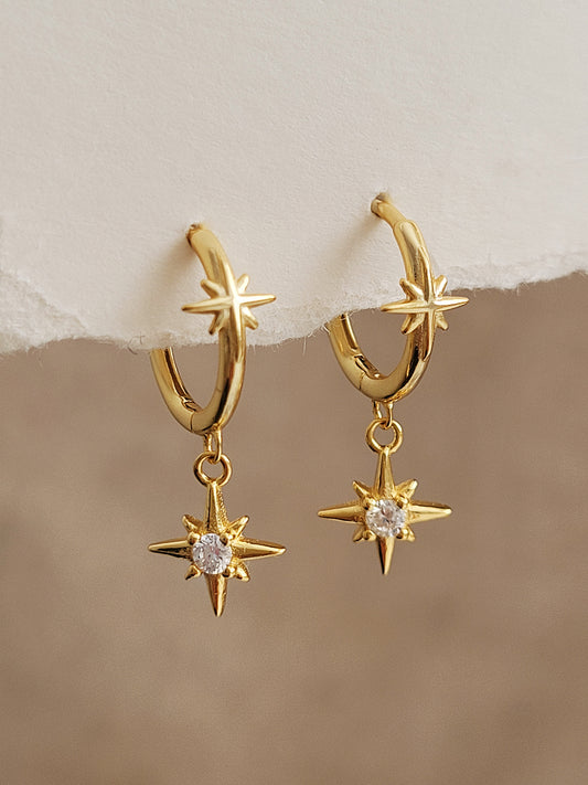 Gold huggie hoop earrings with north star charms on a beige background, crafted in gold plated sterling silver