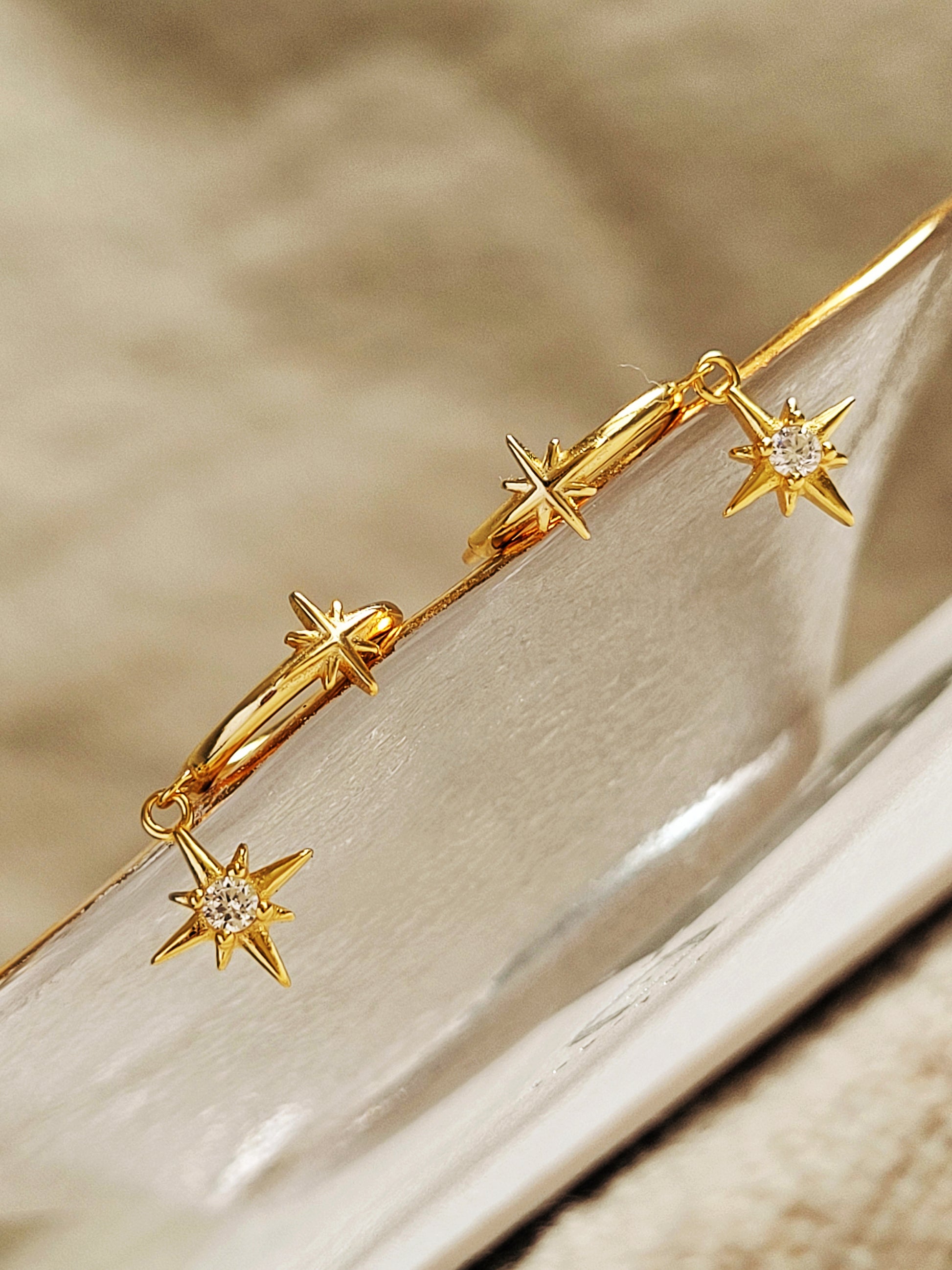 Gold star earrings with dangly north star charms on a neutral background