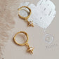 Gold hoop earrings with star charms on a textured beige surface.