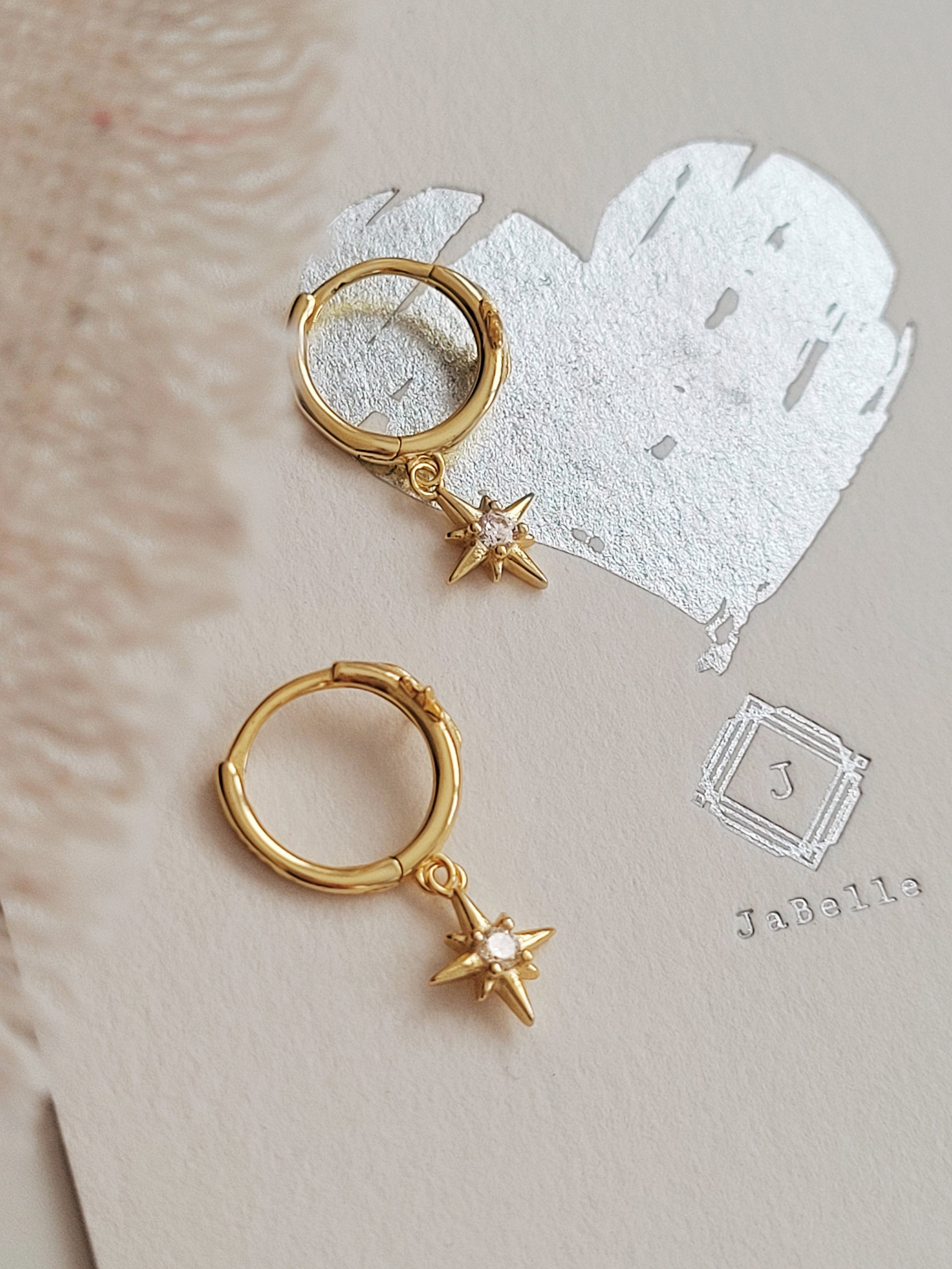 Gold hoop earrings with star charms on a textured beige surface.