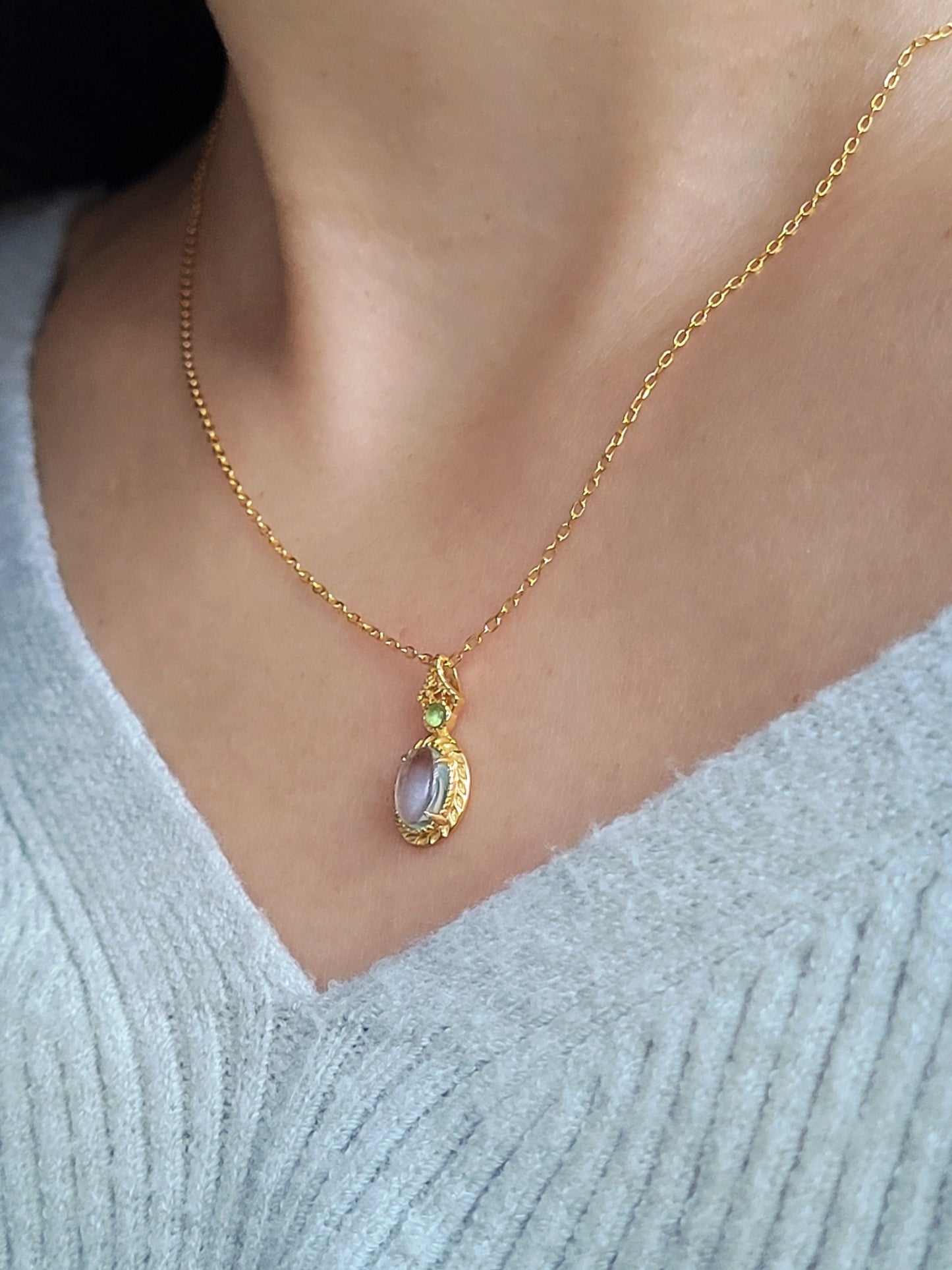 A woman wearing a dainty vintage inspired topaz and gold necklace with a green cubic zirconia.  Perfect anniversary gift for her.