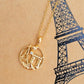 Gold necklace with a Paris-themed pendant on a beige background with a black outline of the Eiffel Tower.