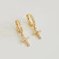 A close-up view of minimalist gold pave cross huggie earrings with sparkling cubic zirconia, displayed on a clean white background.