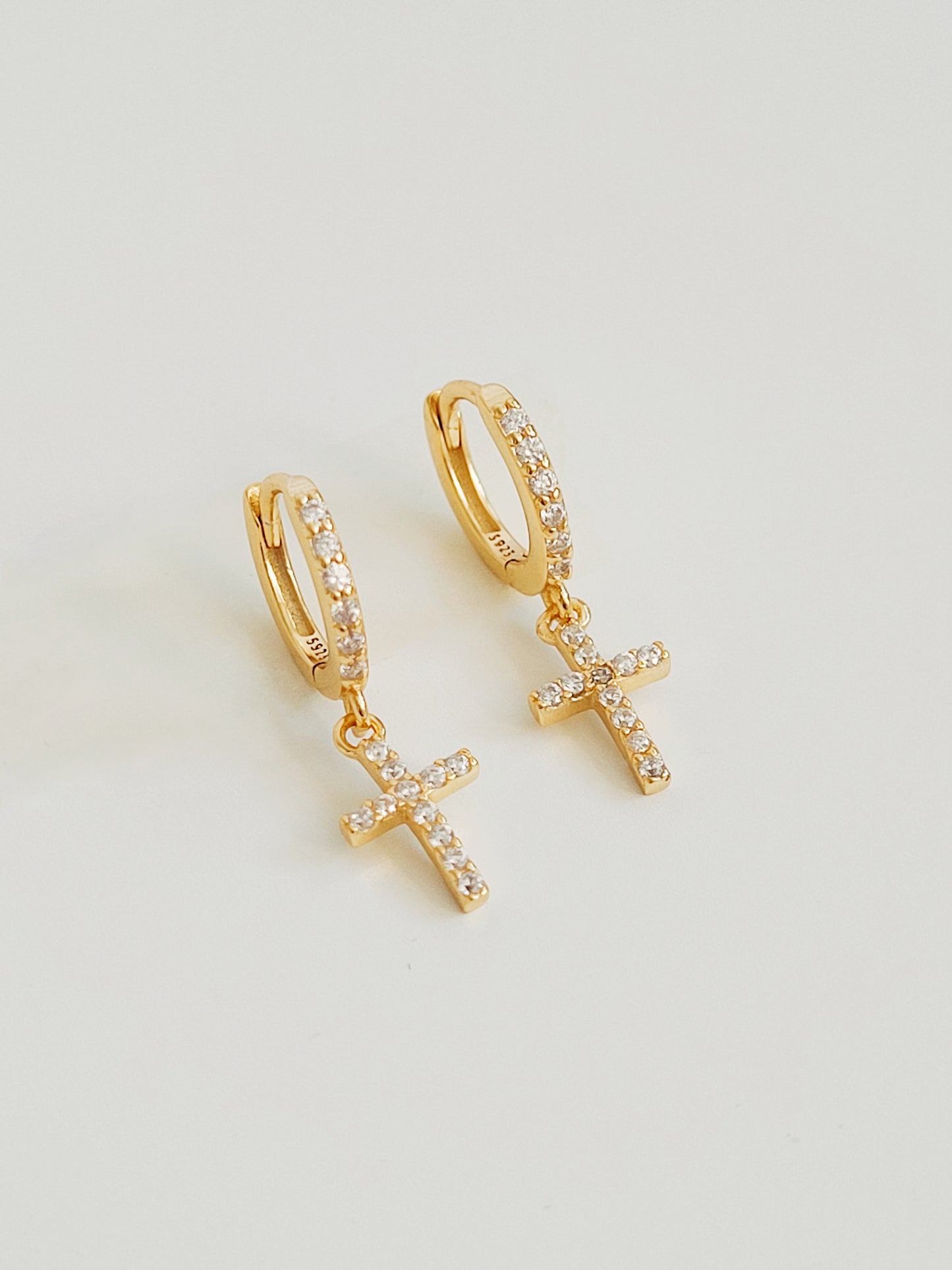 A close-up view of minimalist gold pave cross huggie earrings with sparkling cubic zirconia, displayed on a clean white background.