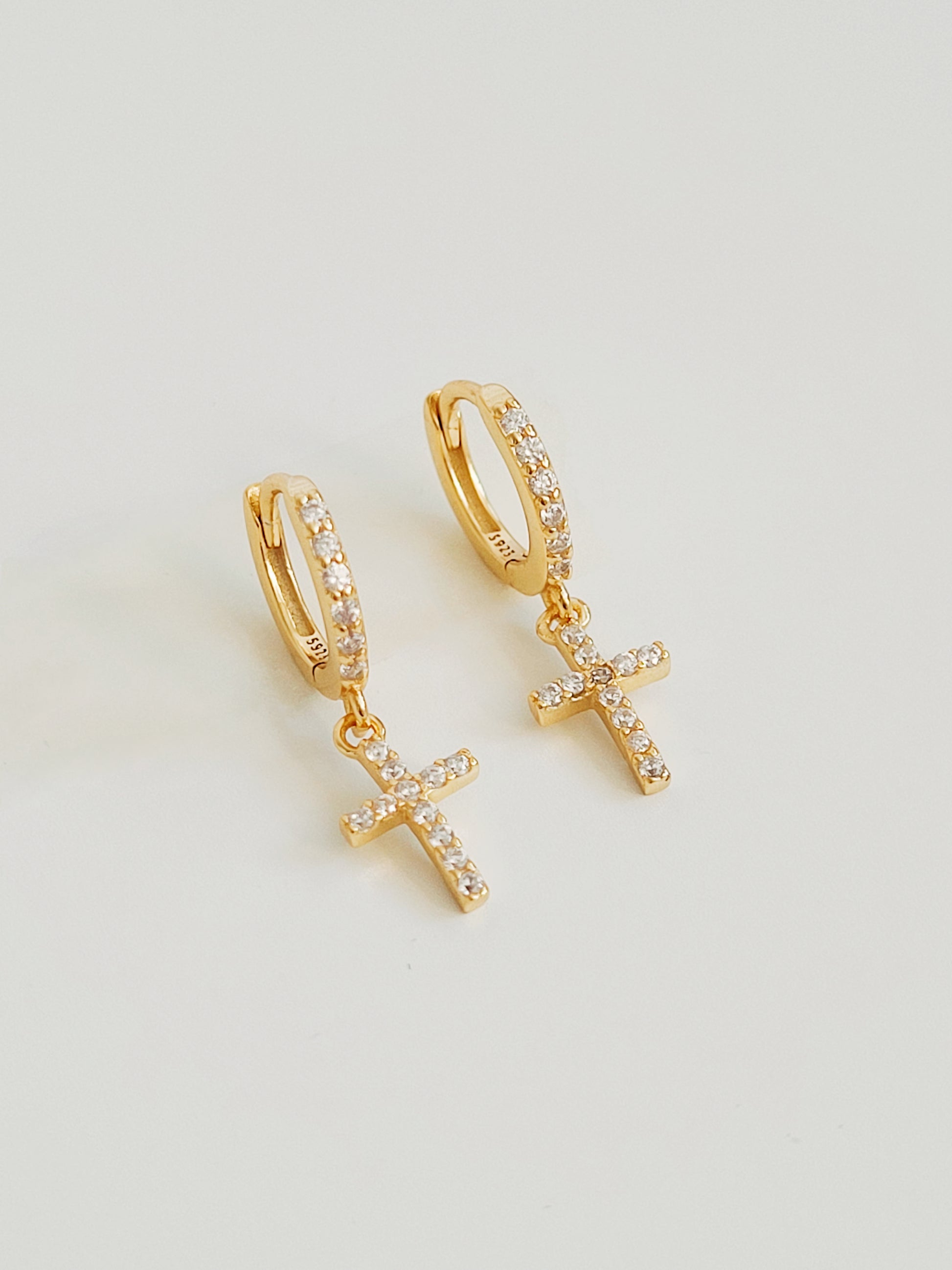 A close-up view of minimalist gold pave cross huggie earrings with sparkling cubic zirconia, displayed on a clean white background.