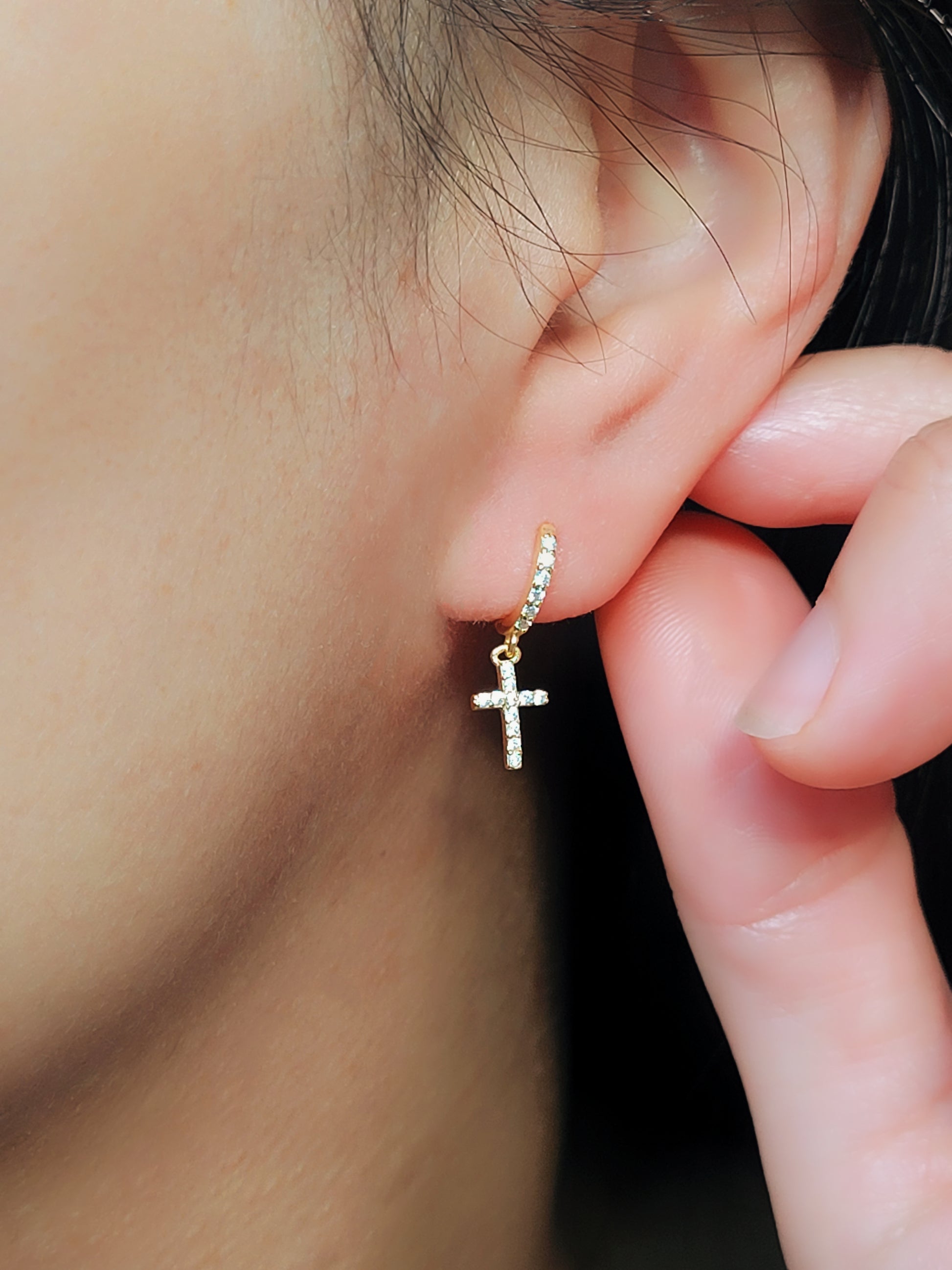 A gold cross earring worn on an ear, showcasing its dainty design and elegant fit, perfect for everyday or special occasions