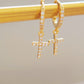 Gold huggie hoop earrings featuring pave-set cubic zirconia crosses, highlighting their intricate craftsmanship on a display.