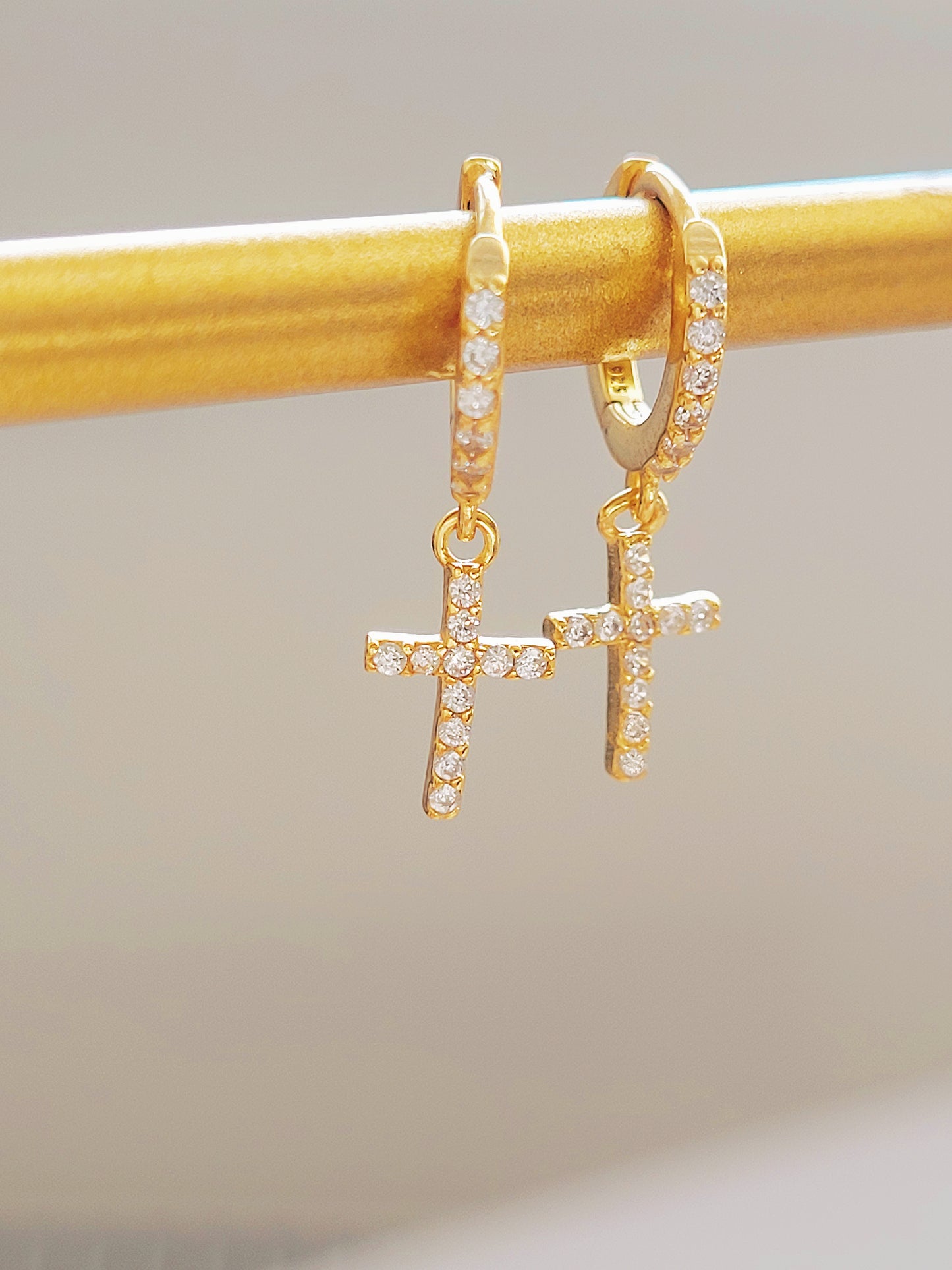 Gold huggie hoop earrings featuring pave-set cubic zirconia crosses, highlighting their intricate craftsmanship on a display.