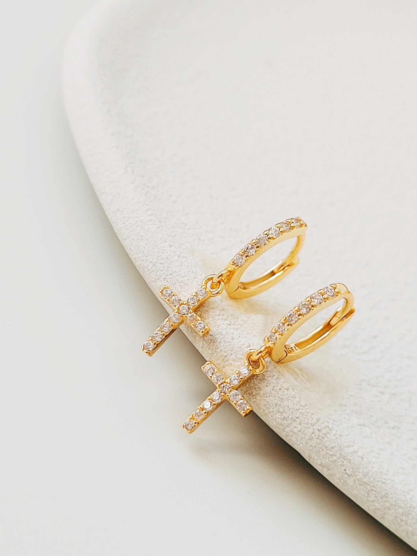 Gold huggie hoop earrings featuring pave-set cubic zirconia crosses, highlighting their intricate craftsmanship on a stone surface.