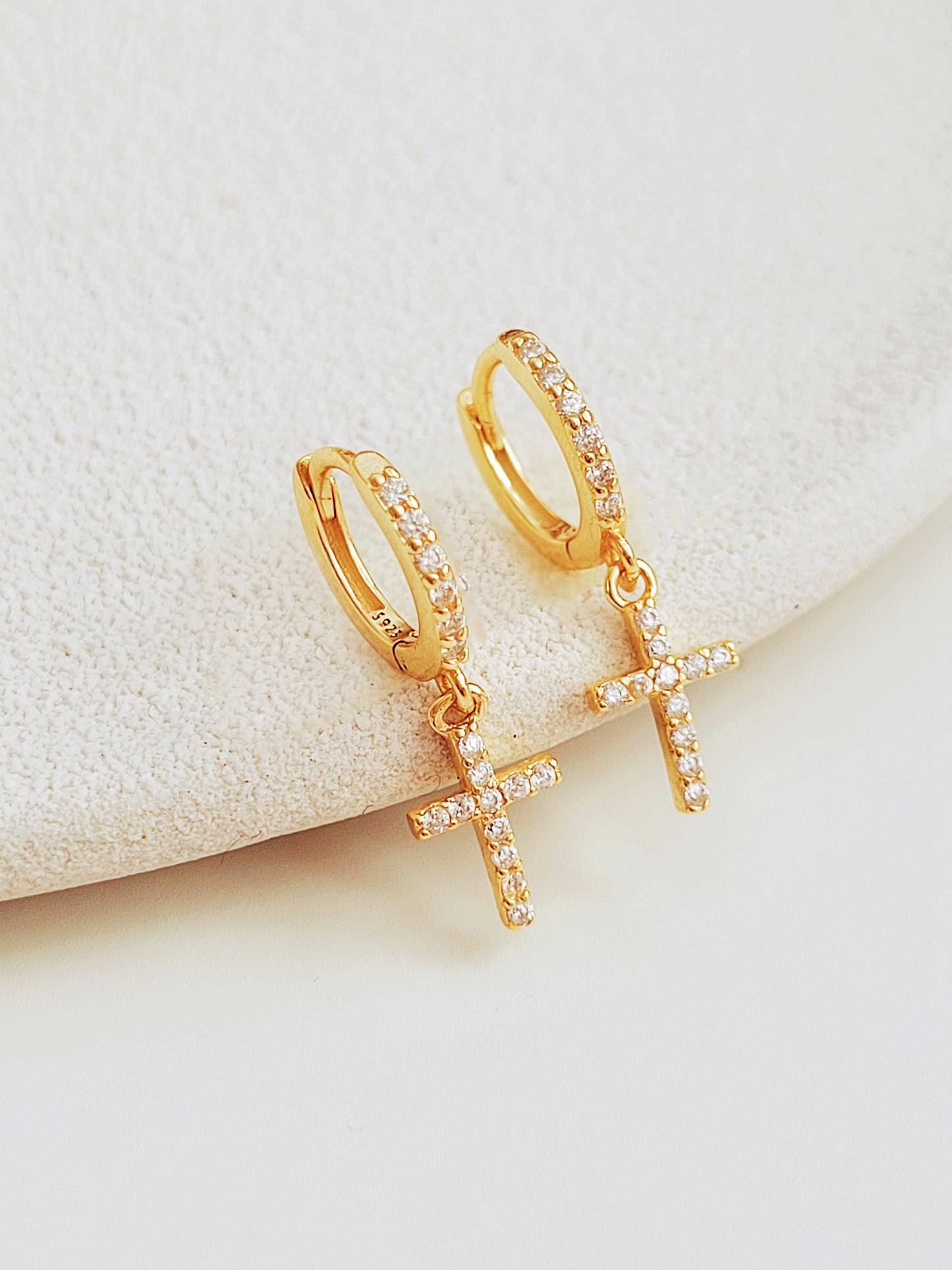 Gold huggie hoop earrings featuring pave-set cubic zirconia crosses, highlighting their intricate craftsmanship on a stone surface.