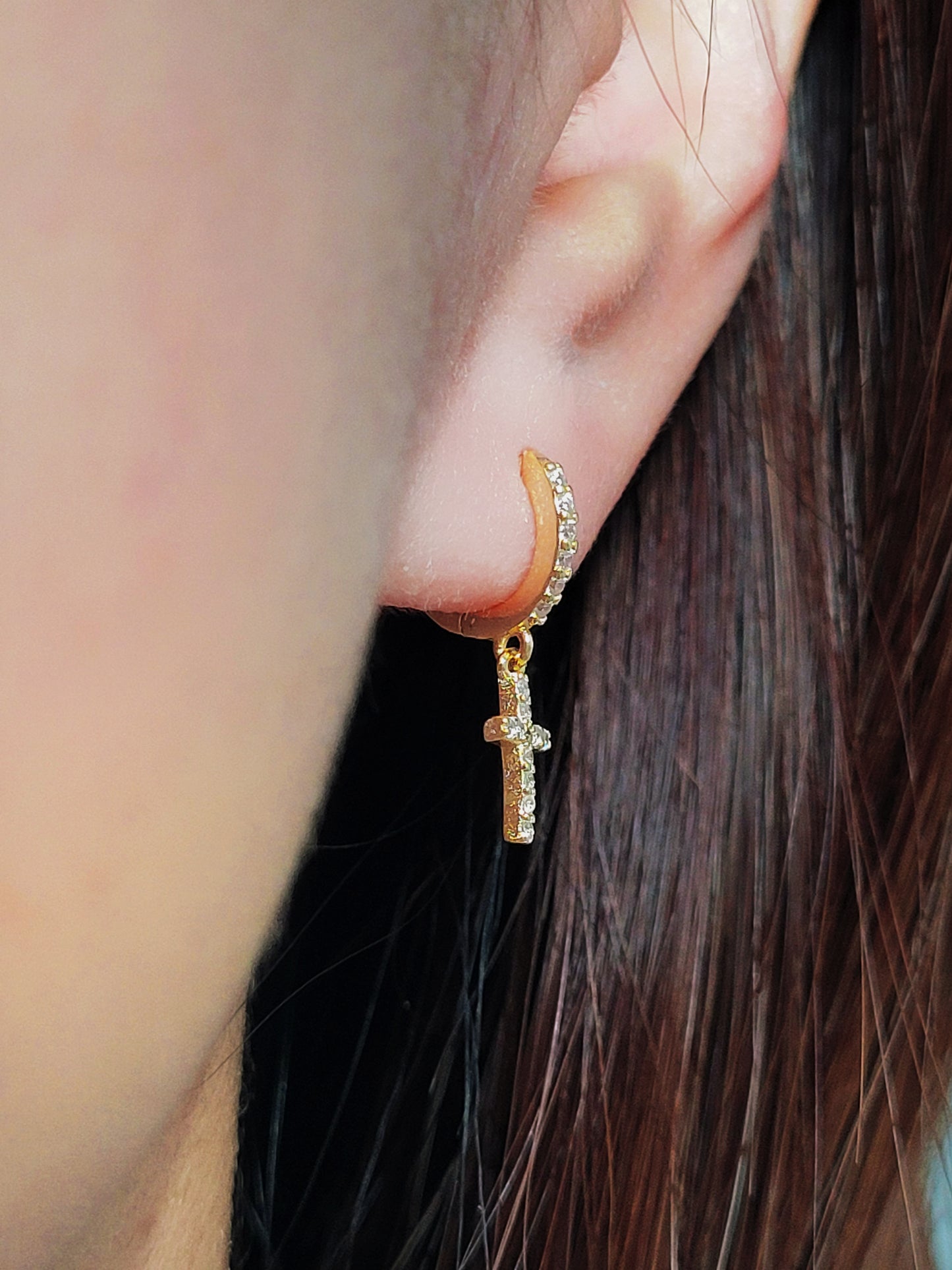 A gold cross earring worn on an ear, showcasing its dainty design and elegant fit, perfect for everyday or special occasions