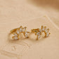 A pair of gold flower huggie earrings featuring floral arrangement shape with cz gemstone, displayed on a luxury beige stone surface.