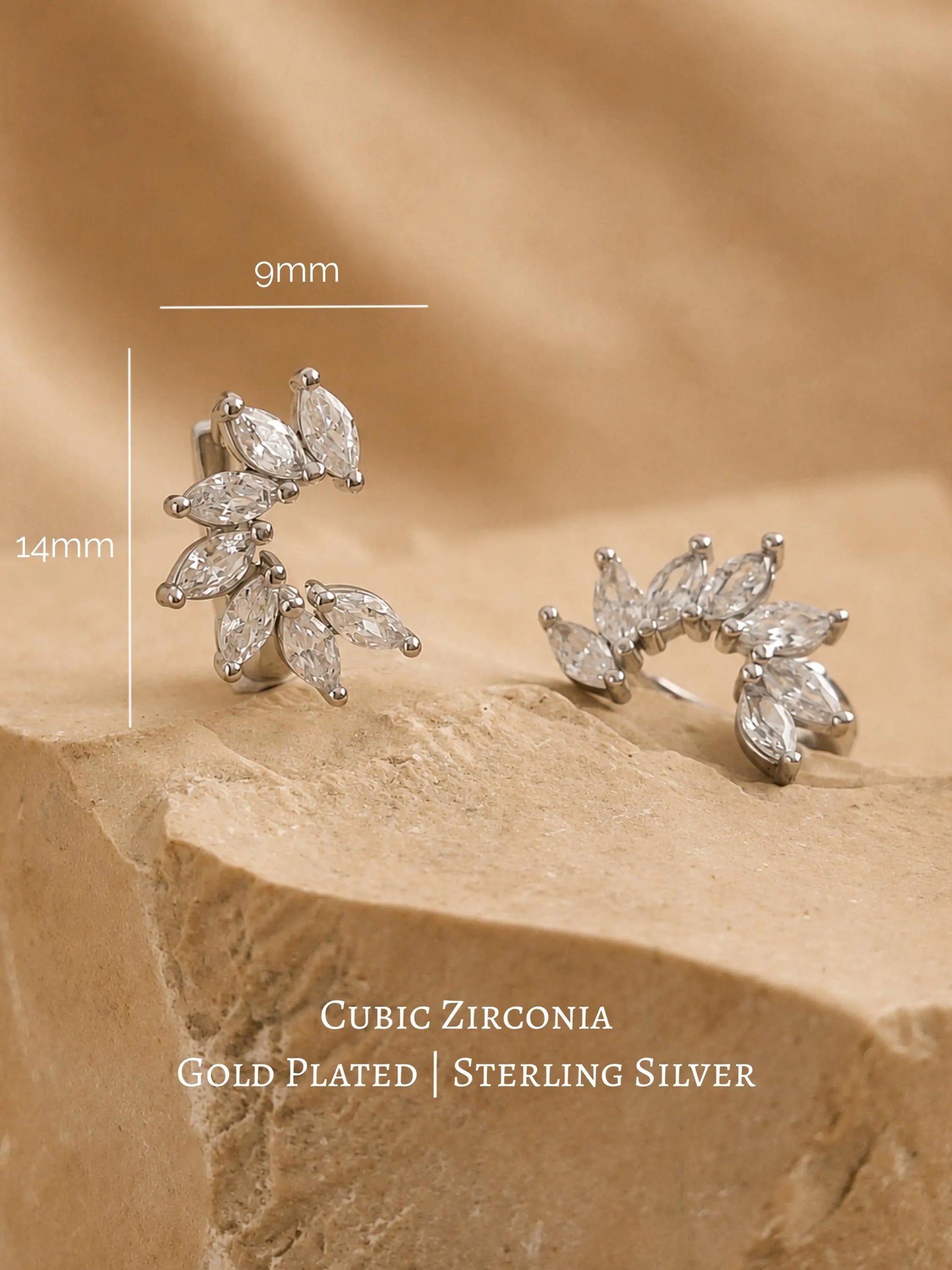 A pair of silver flower huggie earrings featuring floral arrangement shape with cz gemstone, displayed on a luxury beige stone surface.