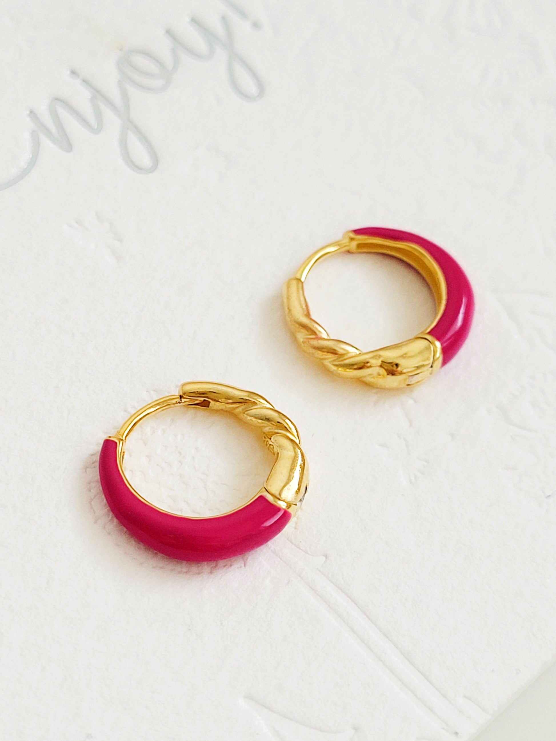 Close-up view of pink and gold enamel hoop earrings featuring twisted gold detail and vibrant green enamel finish.