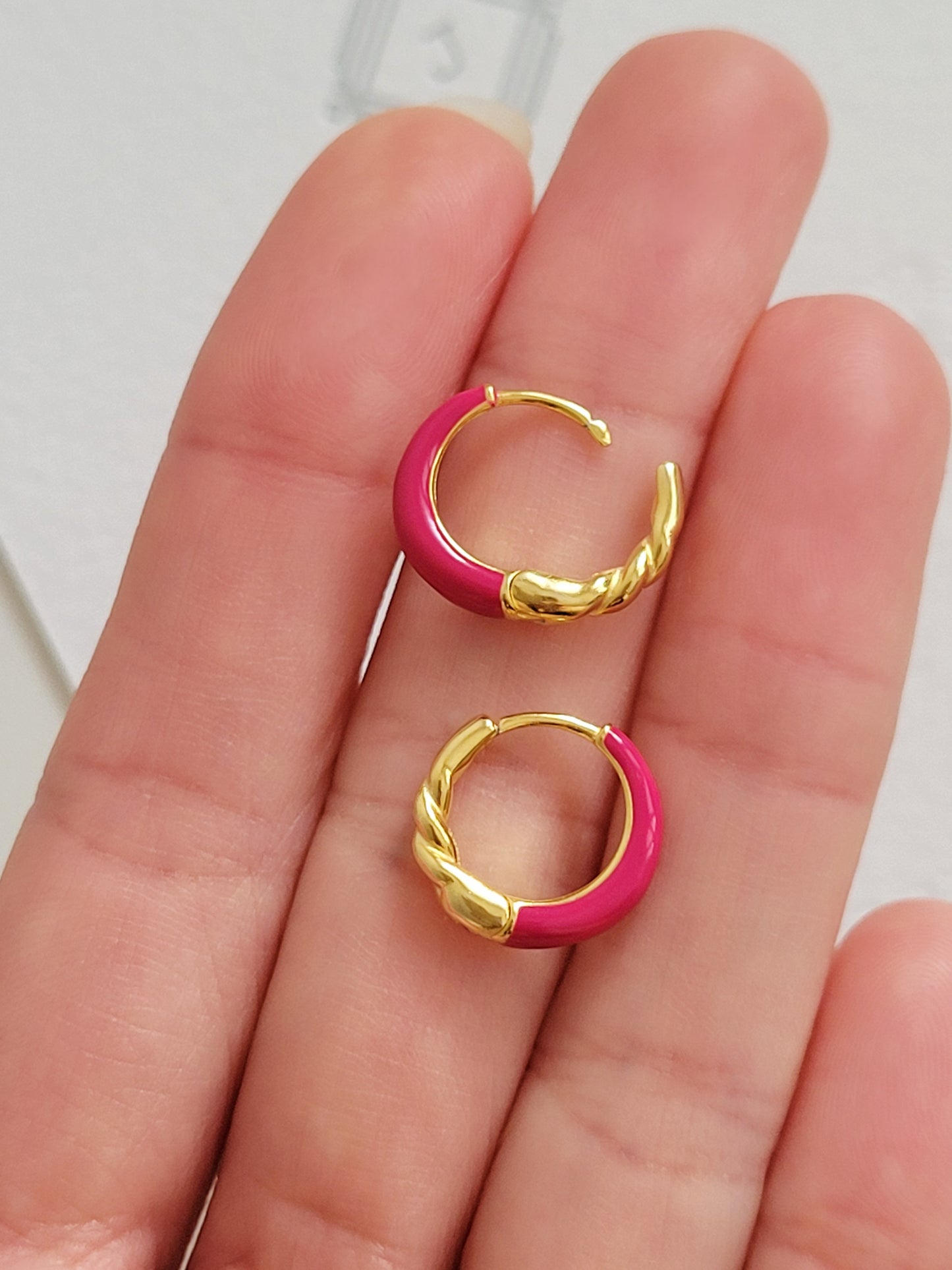 Close-up view of pink and gold enamel hoop earrings featuring twisted gold detail and vibrant green enamel finish.