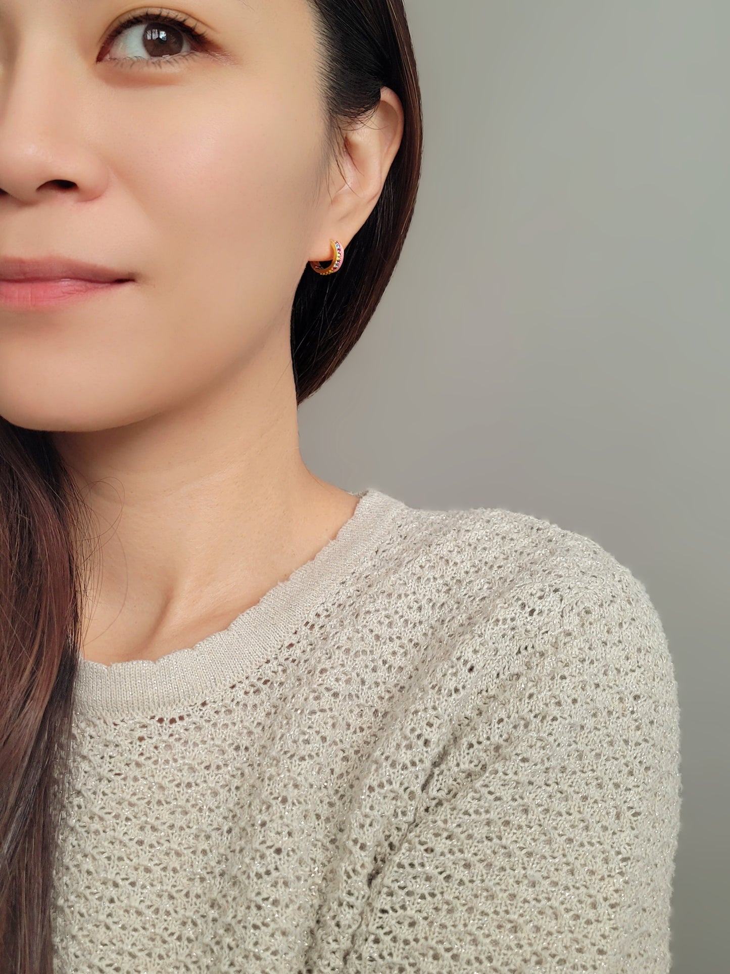 Close up of a woman wearing unique pink enamel hoop earrings with rainbow crystal styled for a boho chic look. Crafted in gold plated sterling silver.