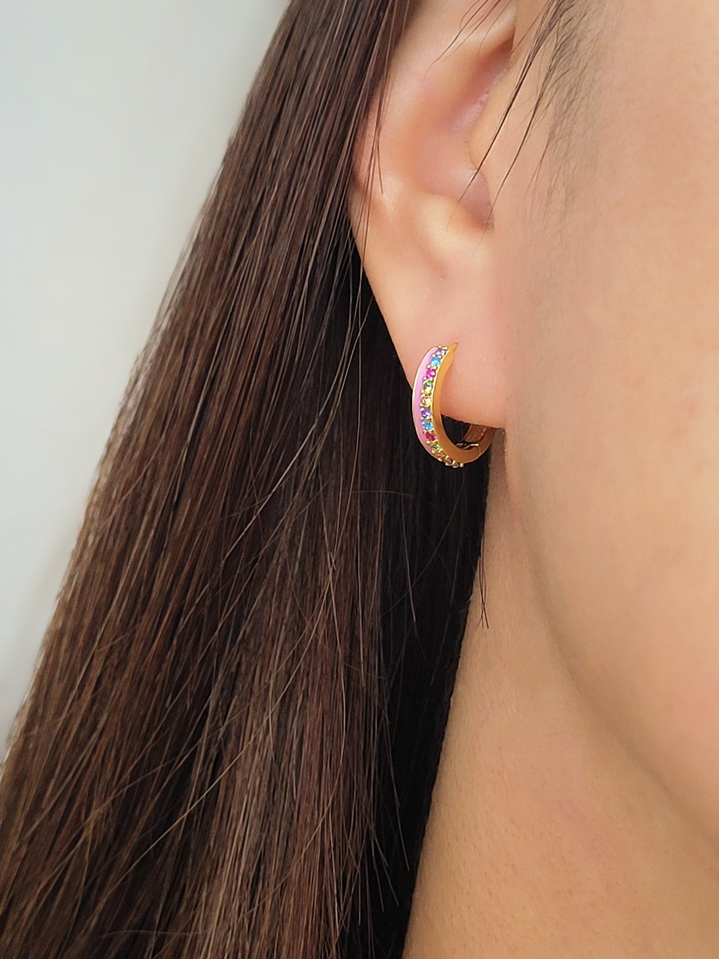 Close up of a woman wearing unique pink enamel hoop earrings with rainbow crystal styled for a boho chic look. Crafted in gold plated sterling silver.