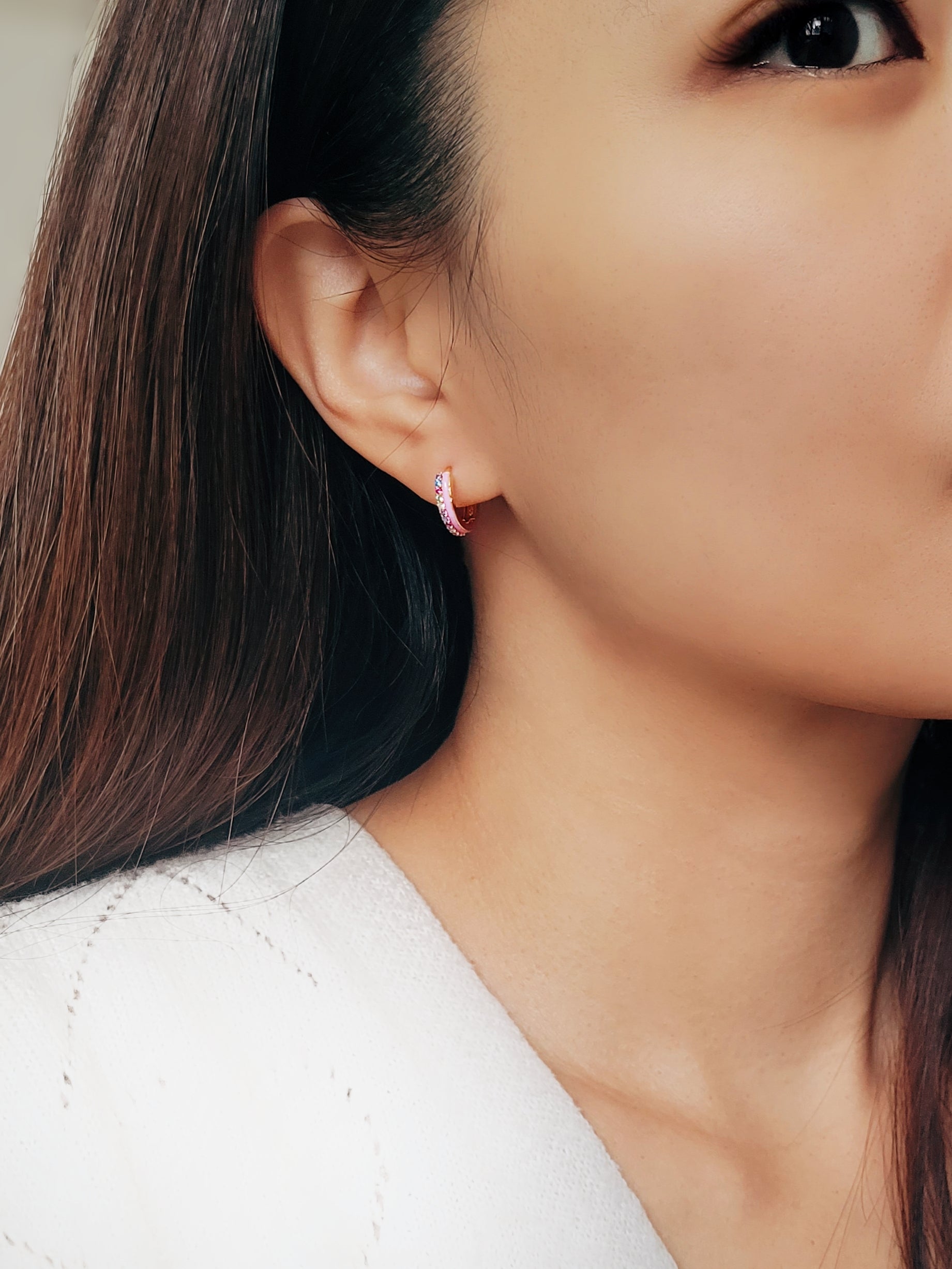 Close up of a woman wearing statement pink enamel hoop earrings with rainbow crystal styled for a boho chic look. Crafted in gold plated sterling silver.