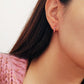 Model wearing pink enamel rainbow huggie hoop earrings with gold finish and multicolor CZ stones, showing small hoop size and elegant fit on ear.