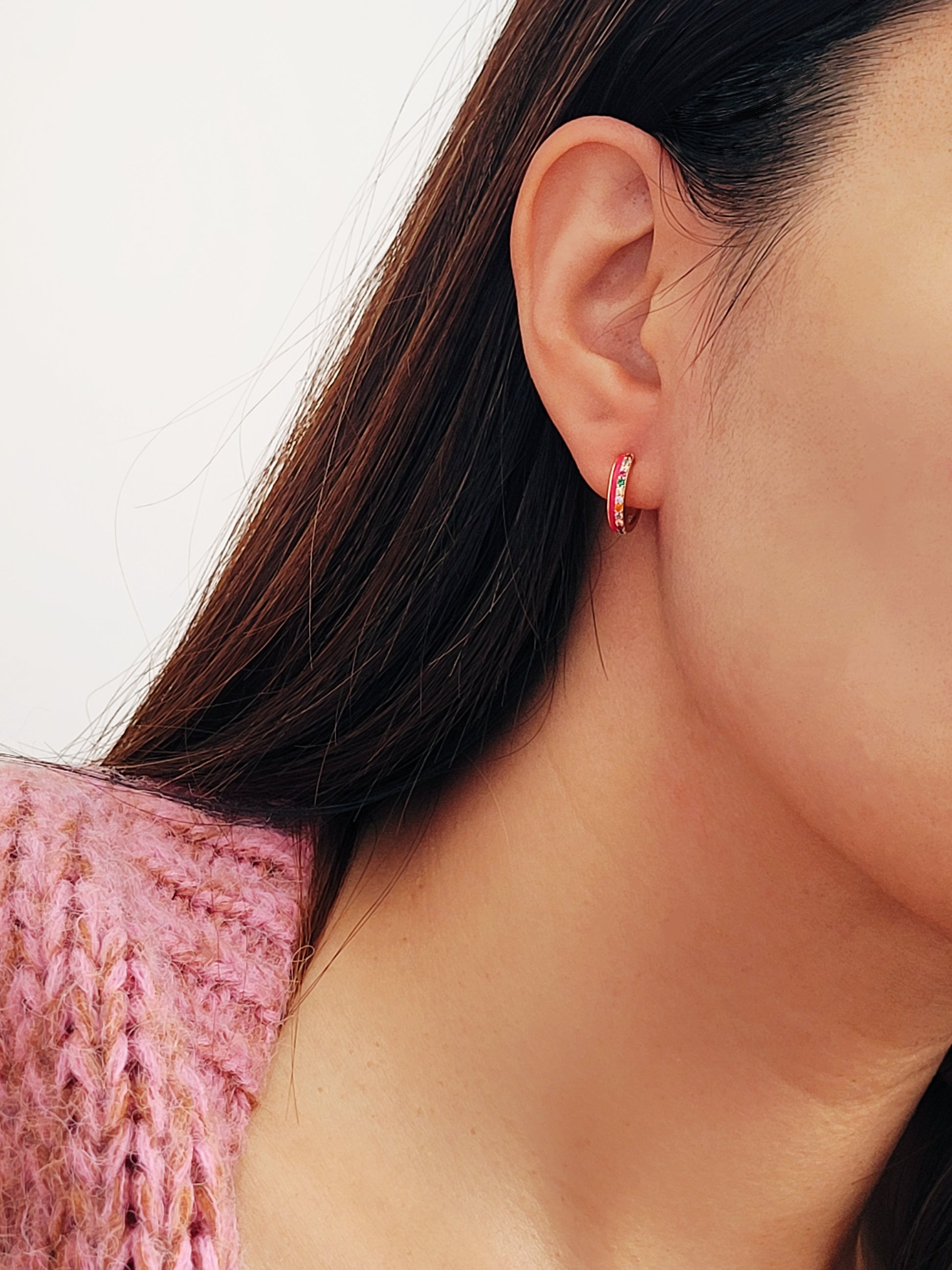 Model wearing pink enamel rainbow huggie hoop earrings with gold finish and multicolor CZ stones, showing small hoop size and elegant fit on ear.