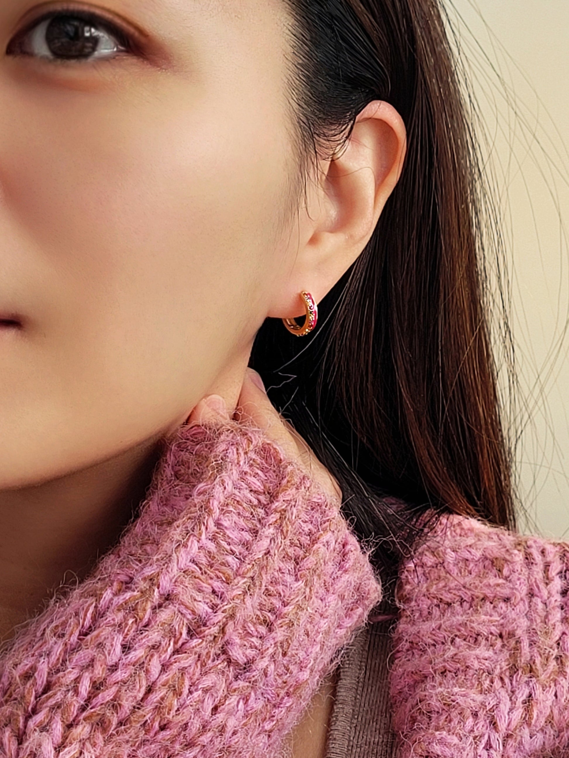 Model wearing pink enamel rainbow huggie hoop earrings with gold finish and multicolor CZ stones, showing small hoop size and elegant fit on ear.