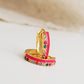 Pair of pink enamel huggie hoop earrings with multicolor cubic zirconia gemstones set in 18k gold plated sterling silver, displayed on a white background.