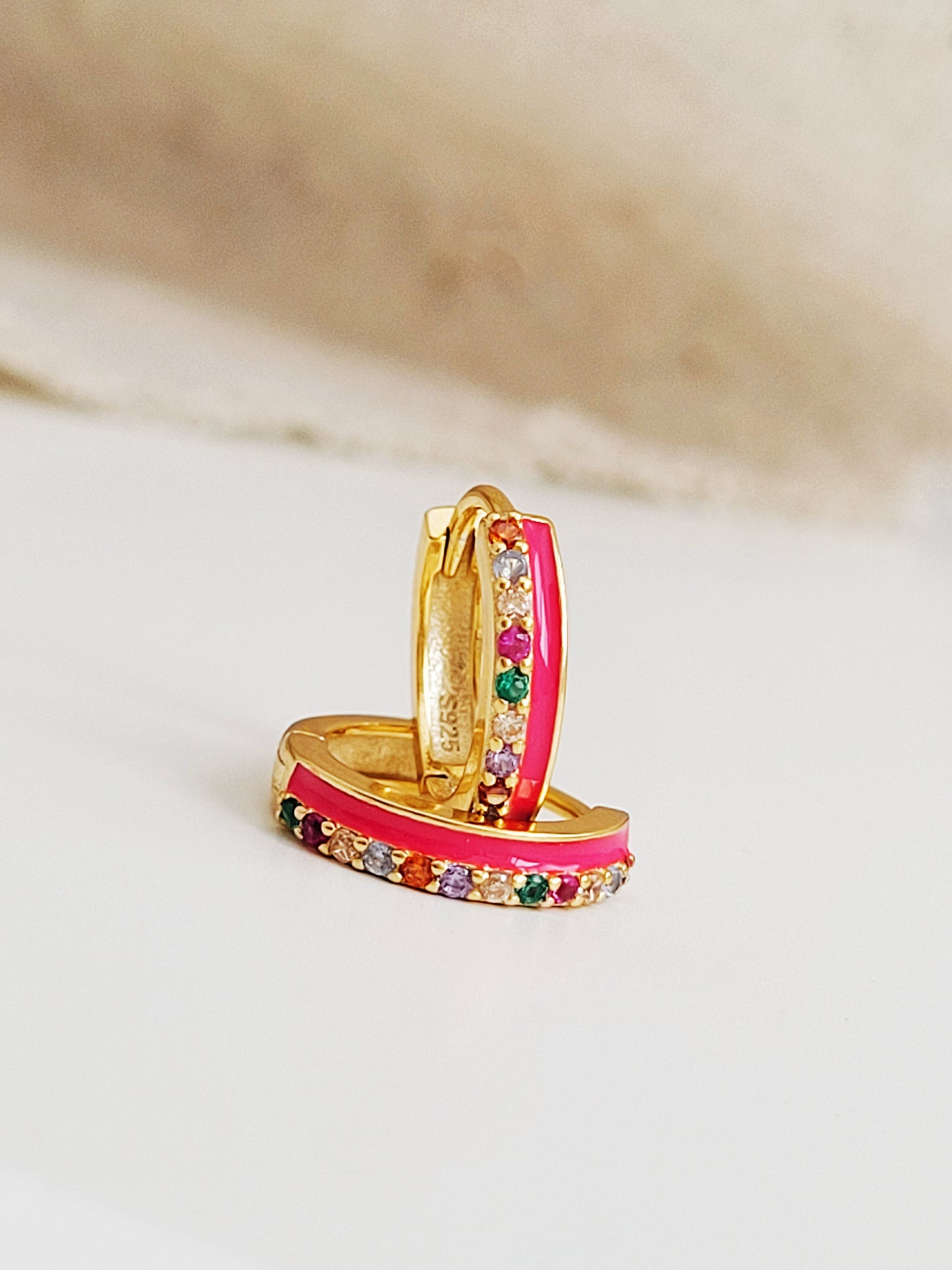 Pair of pink enamel huggie hoop earrings with multicolor cubic zirconia gemstones set in 18k gold plated sterling silver, displayed on a white background.