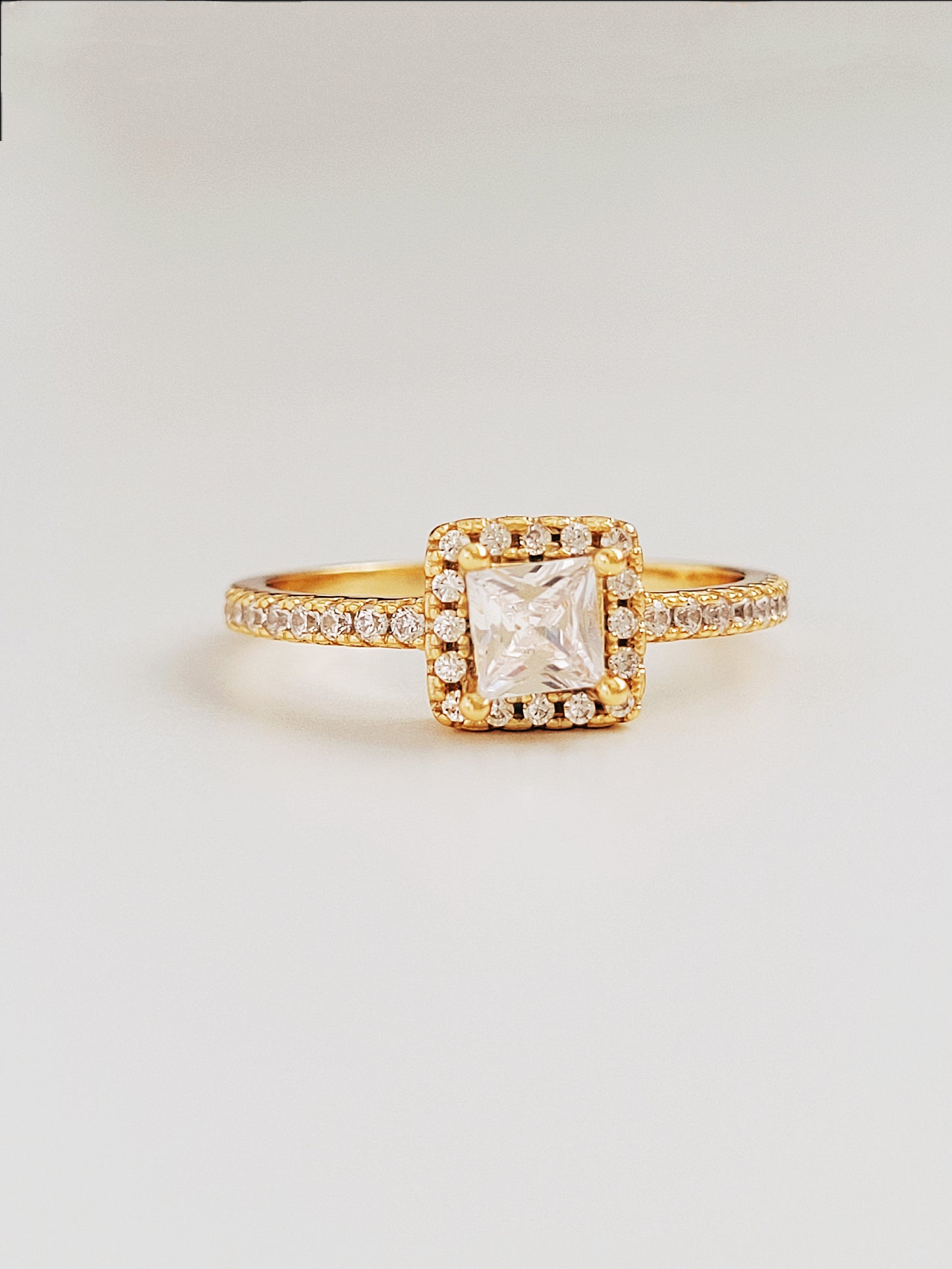 A stunning gold ring featuring a radiant princess square-cut diamond at its center, surrounded by a halo of sparkling smaller diamonds, showing its opulence and intricate craftsmanship.