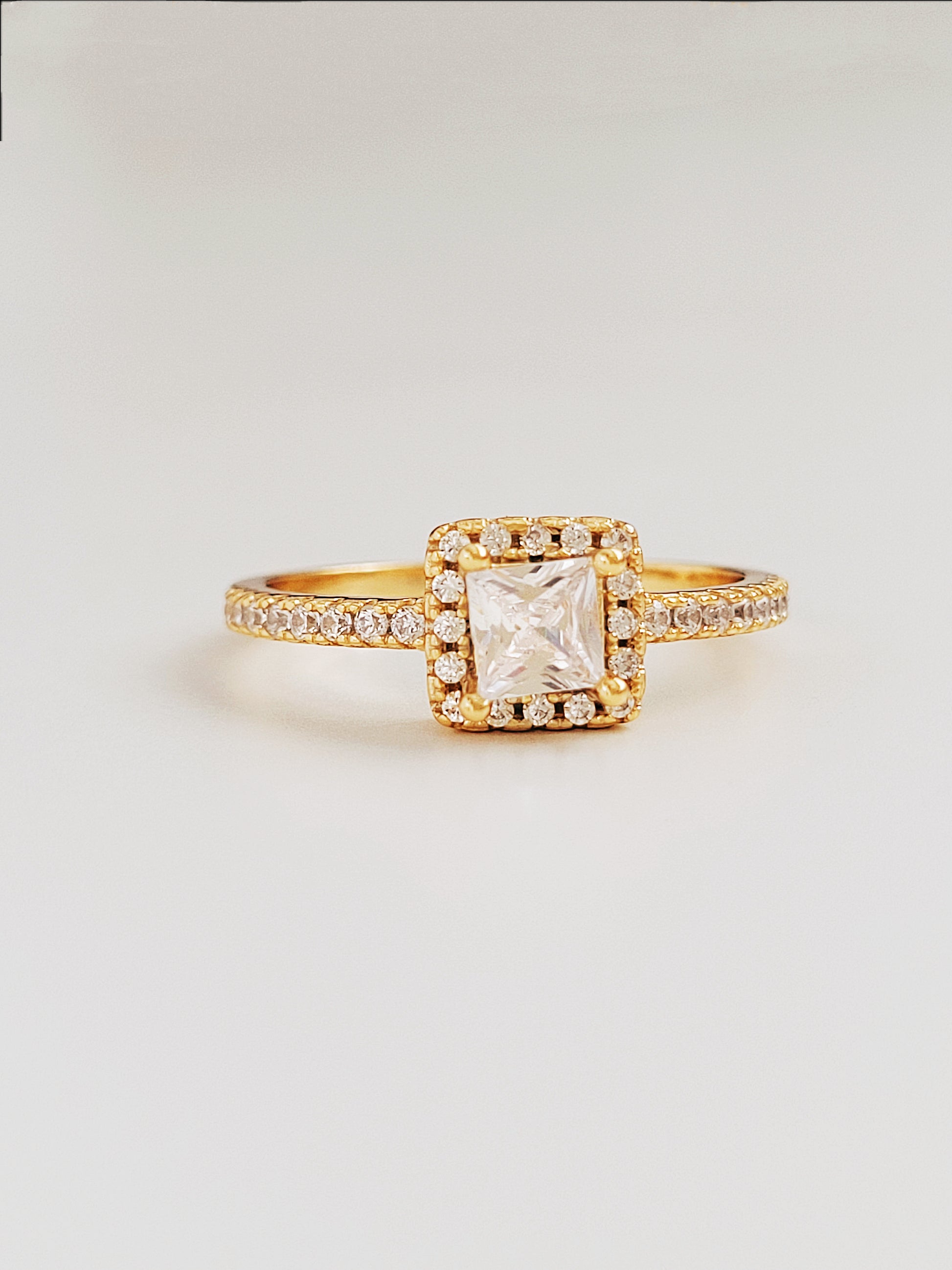 A stunning gold ring featuring a radiant princess square-cut diamond at its center, surrounded by a halo of sparkling smaller diamonds, showing its opulence and intricate craftsmanship.