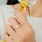 A close-up of a woman's hand holding a champagne glass with an elegant ring showcases a radiant square-cut diamond surrounded by a halo of smaller diamonds, set on a delicate diamond-encrusted gold band.