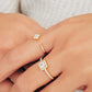A close-up of a woman's hand adorned with elegant rings. One ring showcases a radiant princess cut diamond surrounded by a halo of smaller diamonds, set on a delicate diamond-encrusted gold band.