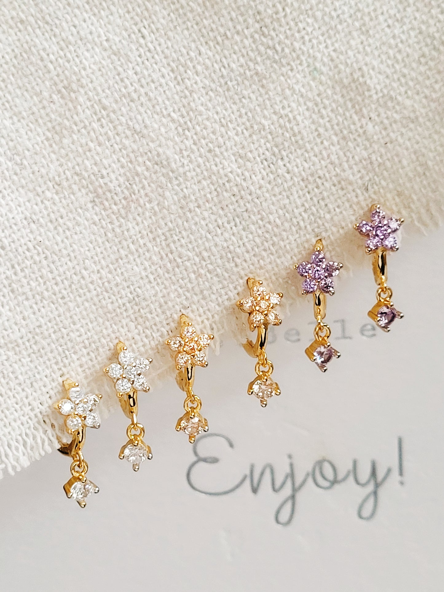 Close-up of a pair of dainty purple flower huggie earrings with dangling charm in 18k gold plated sterling silver and cubic zirconia.