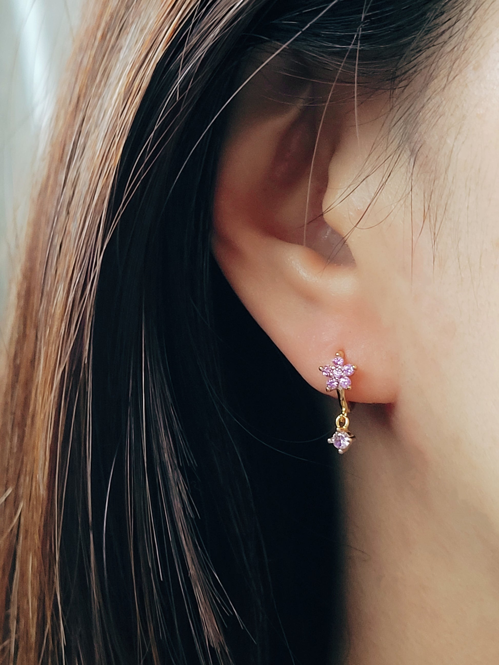 Close-up of a pair of dainty purple flower huggie earrings with dangling charm in 18k gold plated sterling silver and cubic zirconia.