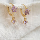 Close-up of a pair of dainty purple flower huggie earrings with dangling charm in 18k gold plated sterling silver and cubic zirconia.
