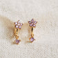 Close-up of a pair of dainty purple flower huggie earrings with dangling charm in 18k gold plated sterling silver and cubic zirconia.