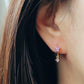 Close-up of a pair of dainty purple flower huggie earrings with dangling charm in 18k gold plated sterling silver and cubic zirconia.